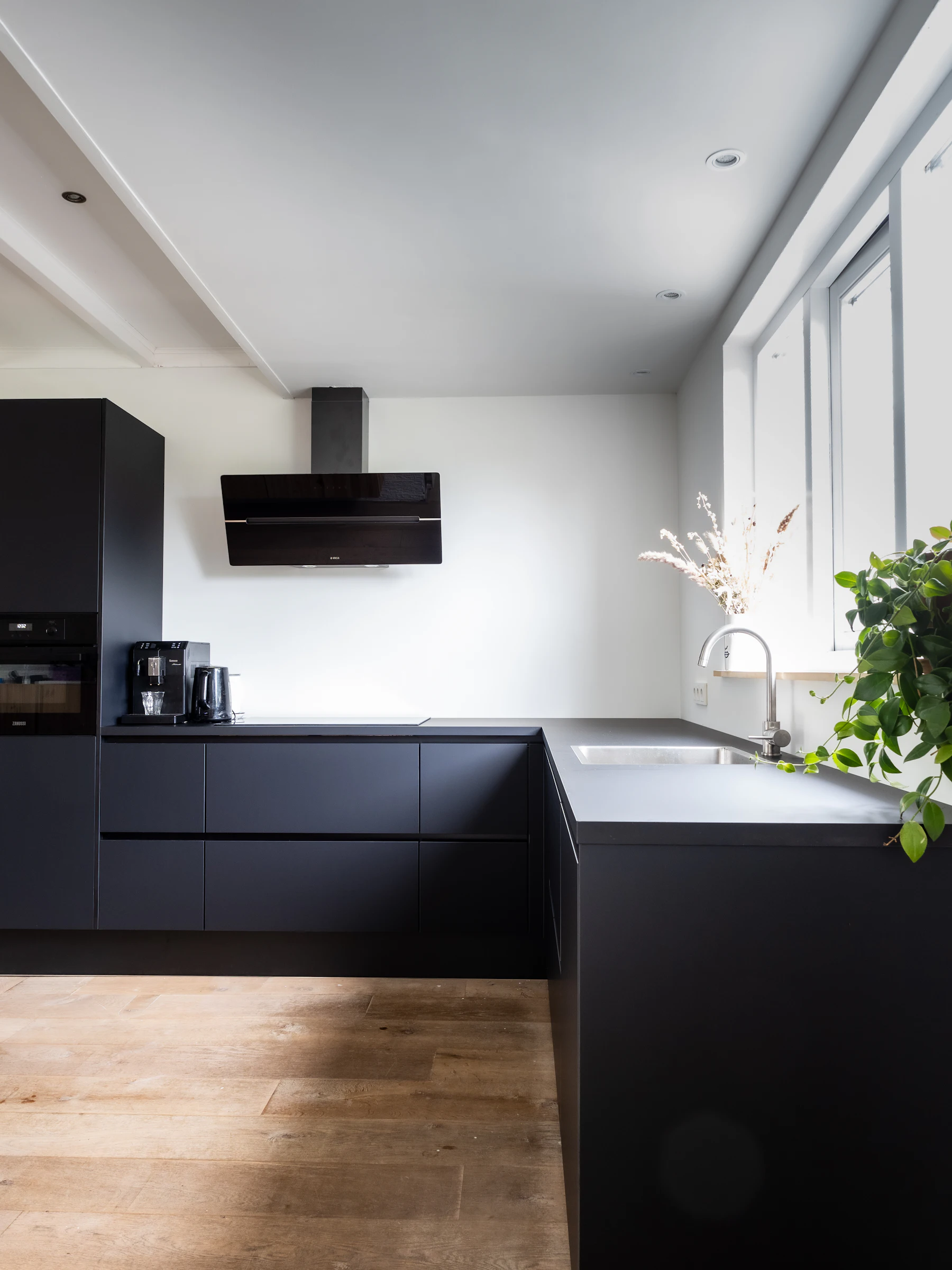A finished kitchen with matte black flat-front cabinets, wood flooring, and a run of wall units