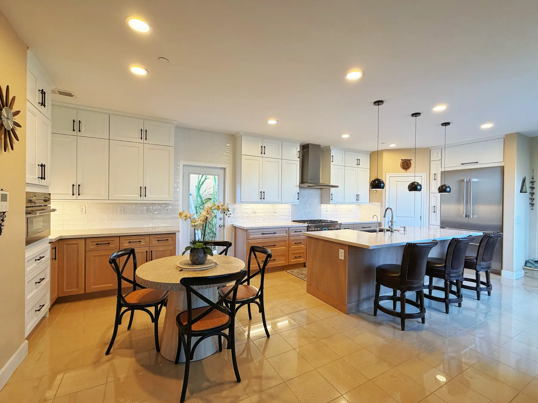 An open kitchen with white uppers and oak bases, a long island with dark leather stools, and a round dining table in the foreground