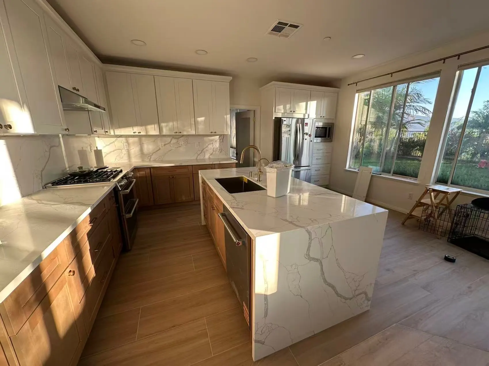 A kitchen with white upper cabinets, timber bases, and an island in heavily veined white stone carried down one end to the floor