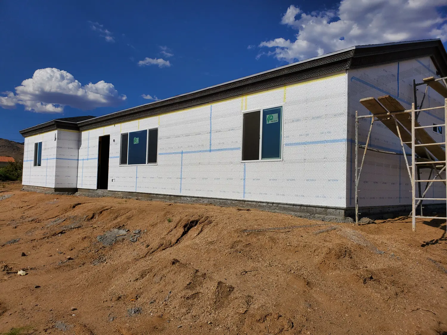 The long side wall of a new build in housewrap with scaffolding standing at the far corner