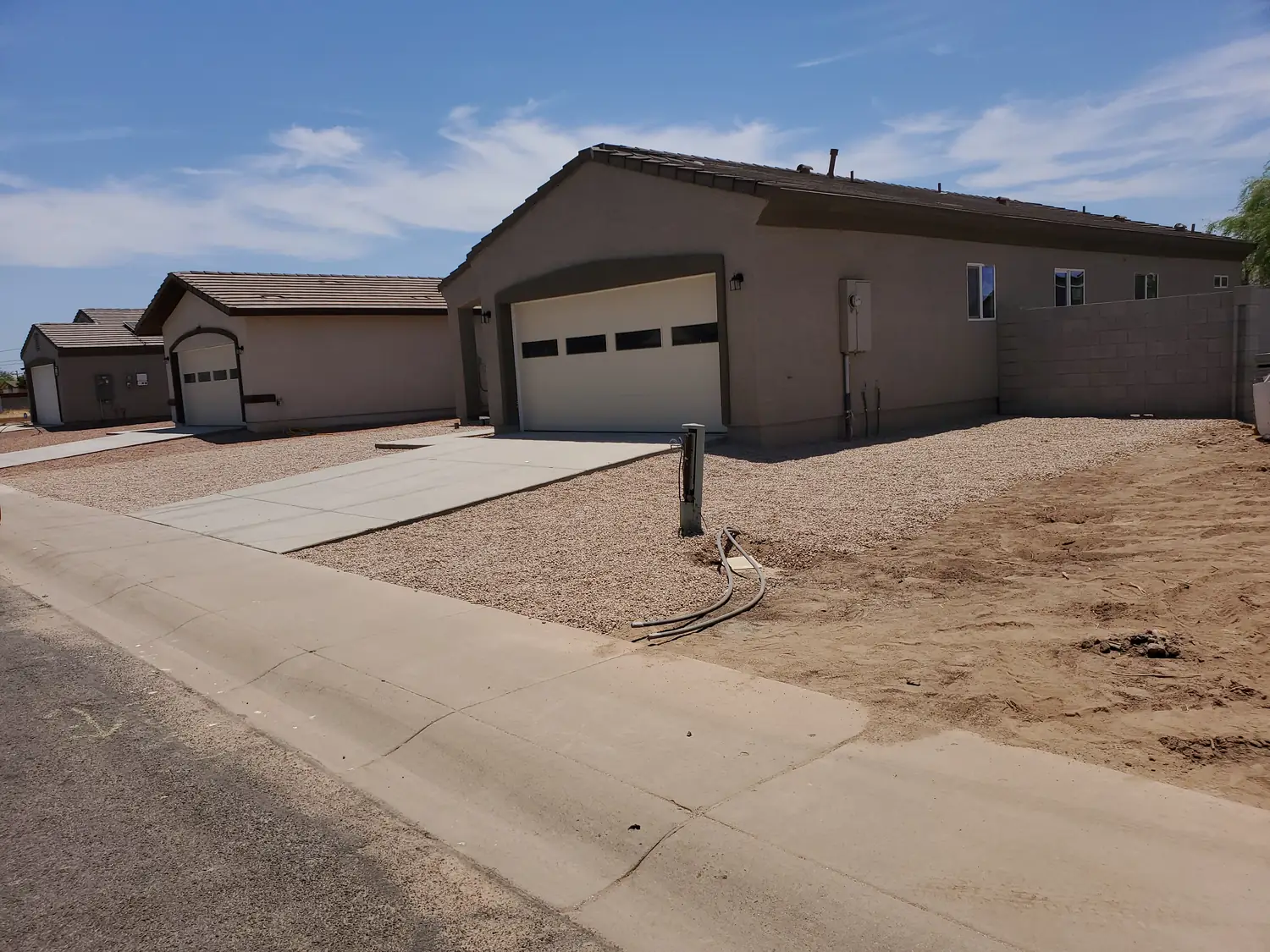 A finished single-story house in stucco with a tiled roof, the garage door fitted and gravel laid up to the boundary wall