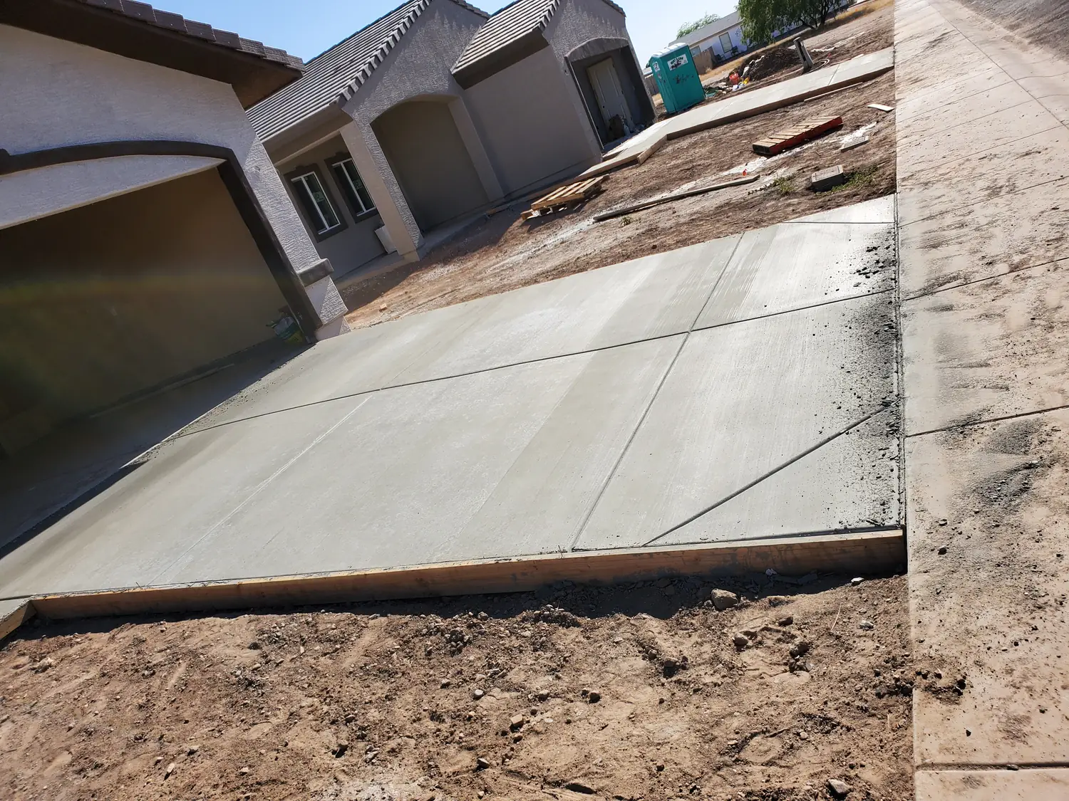 A freshly poured driveway slab still held in its timber forms, running up to the garage of a new house