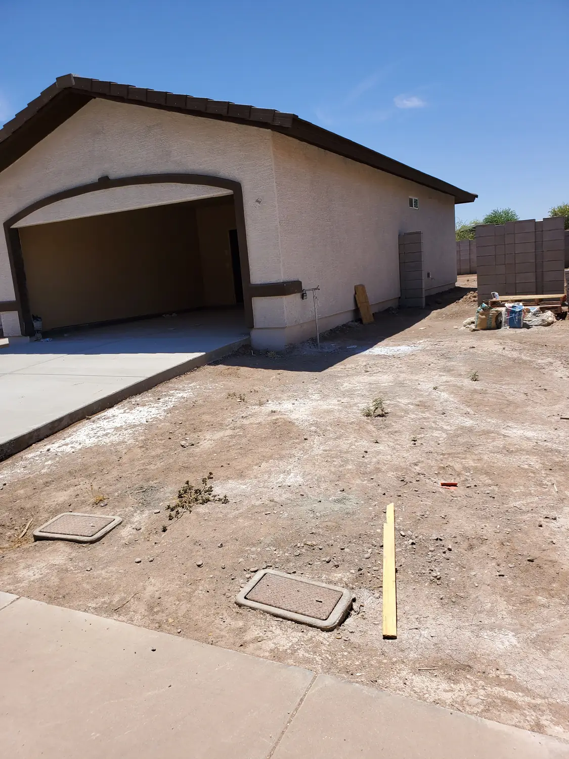 The side of a newly built house with the yard still bare ground and utility covers set into it