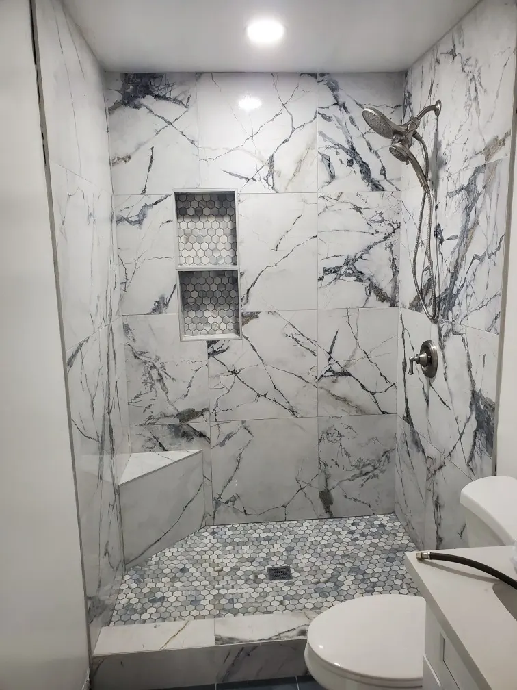 A finished shower lined in large marble-look panels with a hexagonal mosaic niche and floor and a built-in bench